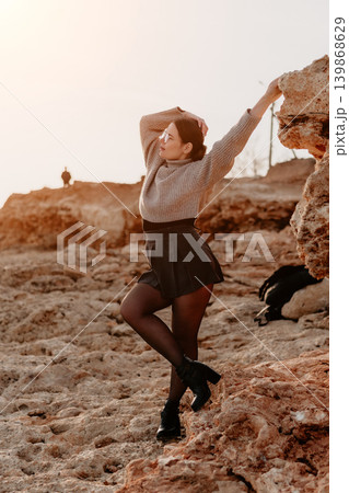 Woman sunset rocky Woman in fashionable winter attire poses on cliffs at golden hour during travel adventure 139868629