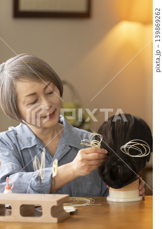 水引で髪飾りを作りマネキンに挿すシニア女性 139869262