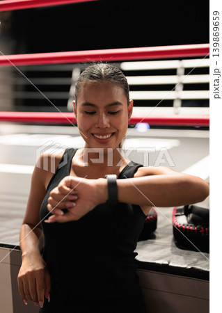 Smiling Female Athlete Checking Smartwatch in Boxing Ring 139869659