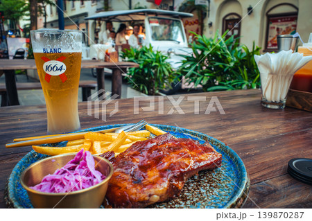 屋外テラスでのランチ。スペアリブとビール、背景を走る観光シャトルカーの風景 屋外テラスでのランチ。スペアリブとビール、背景を走る観光シャトルカーの風景 139870287