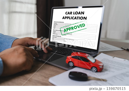 Businessman reviewing approved car loan application on laptop with vehicle model and car key on desk for auto financing, banking approval, credit assessment, and vehicle purchase process. 139870515