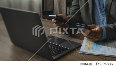Person using smartphone and credit card beside laptop and financial document on office desk for online payment, digital banking, expense management, transaction verification, and remote finance 139870535