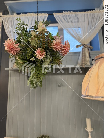 Hanging plant with pink flowers and lush greenery in cozy room interior, suitable as background Hanging plant with pink flowers and lush greenery in cozy room interior, suitable as background 139872572