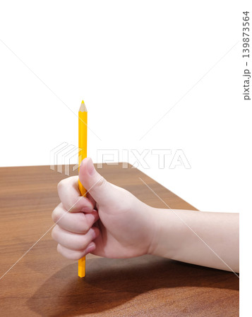 The artist's hand is holding a yellow wooden pencil on a wooden table against a white background. The artist's hand is holding a yellow wooden pencil on a wooden table against a white background. 139873564