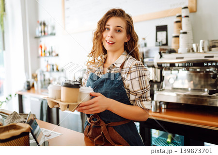 The young barista owner behind the bar gives out to-go orders. Business concept. Drinks to go. 139873701