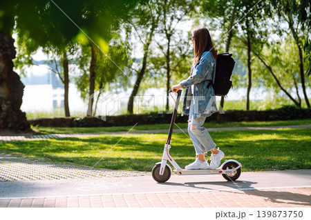 Young female legs on electric scooter. Woman rides electric scooter in park. Active lifestyle. Young female legs on electric scooter. Woman rides electric scooter in park. Active lifestyle. 139873750