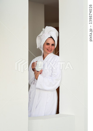 A woman in a robe and towel drinks a hot drink on a terrace after a shower 139874016