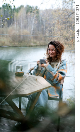 A sweet woman with curly hair drinks tea and relaxes on the terrace of her house on an autumn day. Health care, sincerity, a sense of balance and calm. A sweet woman with curly hair drinks tea and relaxes on the terrace of her house on an autumn day. Health care, sincerity, a sense of balance and calm. 139874371