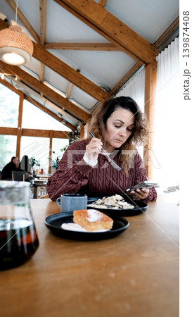 A young woman eats pasta in a restaurant and texts on her smartphone. 139874408