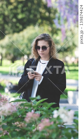 Caucasian woman with curly hair using her mobile phone outdoors. Close-up. Communication technology and modern lifestyle concept 139874424