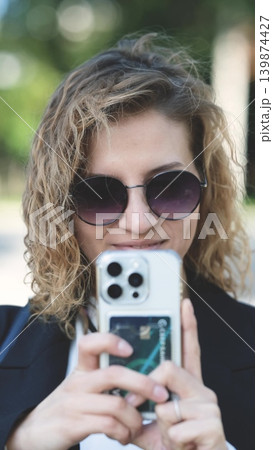 Caucasian woman with curly hair using her mobile phone outdoors. Close-up. Communication technology and modern lifestyle concept 139874427