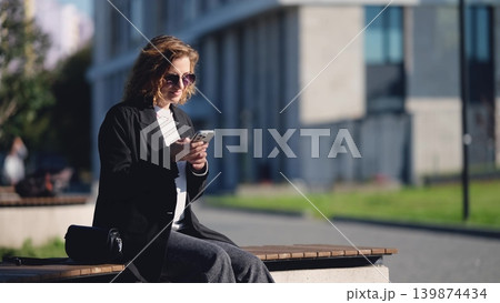 Caucasian woman with curly hair using her mobile phone outdoors. Close-up. Communication technology and modern lifestyle concept Caucasian woman with curly hair using her mobile phone outdoors. Close-up. Communication technology and modern lifestyle concept 139874434
