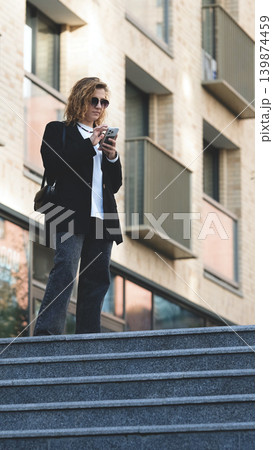 Caucasian woman with curly hair using her mobile phone outdoors. Close-up. Communication technology and modern lifestyle concept Caucasian woman with curly hair using her mobile phone outdoors. Close-up. Communication technology and modern lifestyle concept 139874459