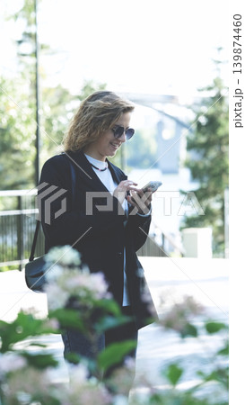 Caucasian woman with curly hair using her mobile phone outdoors. Close-up. Communication technology and modern lifestyle concept 139874460