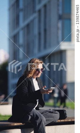 Caucasian woman with curly hair using her mobile phone outdoors. Close-up. Communication technology and modern lifestyle concept Caucasian woman with curly hair using her mobile phone outdoors. Close-up. Communication technology and modern lifestyle concept 139874465
