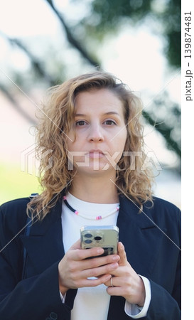 Caucasian woman with curly hair using her mobile phone outdoors. Close-up. Communication technology and modern lifestyle concept 139874481