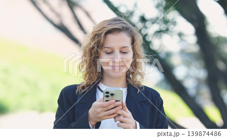 Caucasian woman with curly hair using her mobile phone outdoors. Close-up. Communication technology and modern lifestyle concept Caucasian woman with curly hair using her mobile phone outdoors. Close-up. Communication technology and modern lifestyle concept 139874486