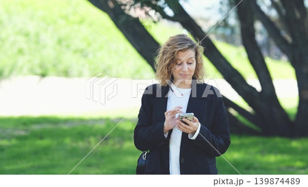 Caucasian woman with curly hair using her mobile phone outdoors. Close-up. Communication technology and modern lifestyle concept Caucasian woman with curly hair using her mobile phone outdoors. Close-up. Communication technology and modern lifestyle concept 139874489