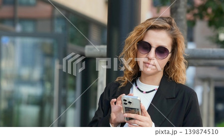 Caucasian woman with curly hair using her mobile phone outdoors. Close-up. Communication technology and modern lifestyle concept Caucasian woman with curly hair using her mobile phone outdoors. Close-up. Communication technology and modern lifestyle concept 139874510