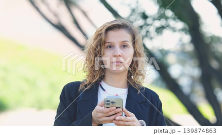 Caucasian woman with curly hair using her mobile phone outdoors. Close-up. Communication technology and modern lifestyle concept 139874863