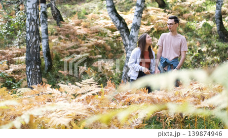 Married couple relaxing in nature during a walk in the autumn forest. Woman and man in love walking through tall yellow grass, in fern leaves Married couple relaxing in nature during a walk in the autumn forest. Woman and man in love walking through tall yellow grass, in fern leaves 139874946