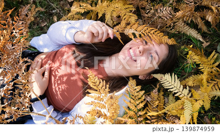 Cheerful young woman lies on yellow autumn leaves in the park and smiles. 139874959