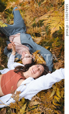 A woman and a man in love lie in tall yellow grass, in fern leaves. The married couple relaxes in nature during a walk in the autumn forest. A woman and a man in love lie in tall yellow grass, in fern leaves. The married couple relaxes in nature during a walk in the autumn forest. 139874995