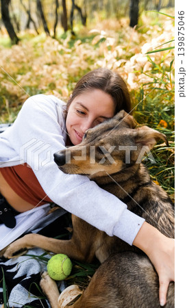 Young woman relaxes while walking her dog in autumn forest Young woman relaxes while walking her dog in autumn forest 139875046