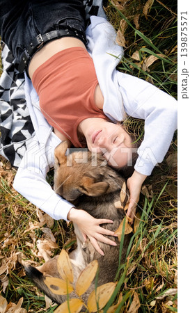 Young woman relaxes while walking her dog in autumn forest Young woman relaxes while walking her dog in autumn forest 139875571