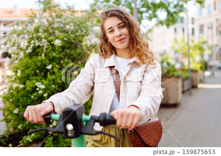 Happy woman rides electric scooter at weekend leisure time. Ecological transport. Active lifestyle. Happy woman rides electric scooter at weekend leisure time. Ecological transport. Active lifestyle. 139875653