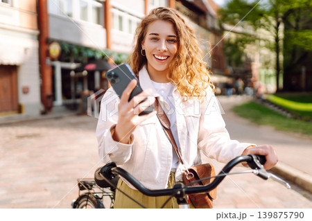 Woman using mobile phone, walks with bicycle, looks around at beautiful architecture. Selfie time. Woman using mobile phone, walks with bicycle, looks around at beautiful architecture. Selfie time. 139875790