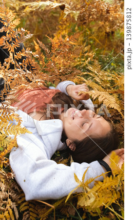Cheerful young woman lies on yellow autumn leaves in the park and smiles. Cheerful young woman lies on yellow autumn leaves in the park and smiles. 139875812
