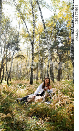 A sweet young woman with her dog enjoys the beauty of nature and the bond with her pets. The woman drinks tea from a thermos A sweet young woman with her dog enjoys the beauty of nature and the bond with her pets. The woman drinks tea from a thermos 139875965