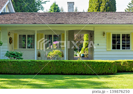 White Residential House Facade with Yellow Shutters and Trim Behind a Green Hedge 139876250