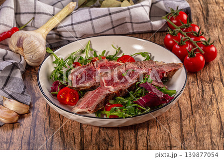 Grilled beef steak slices on fresh arugula salad with cherry tomatoes, rustic wooden table background, gourmet food photography Grilled beef steak slices on fresh arugula salad with cherry tomatoes, rustic wooden table background, gourmet food photography 139877054