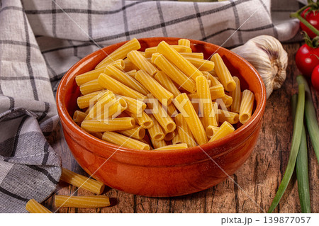 Dry pasta in terracotta bowl with fresh ingredients. Rigatoni, tomatoes, garlic, green onions on rustic wooden table Dry pasta in terracotta bowl with fresh ingredients. Rigatoni, tomatoes, garlic, green onions on rustic wooden table 139877057