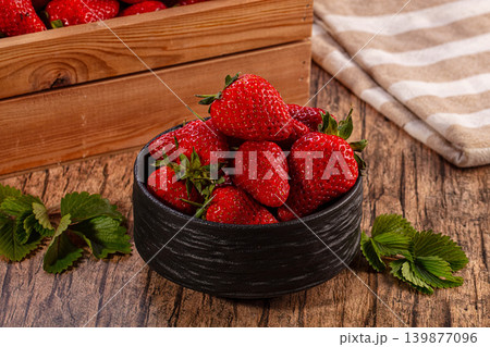 Ripe red strawberries in black bowl and wooden crate on rustic table Ripe red strawberries in black bowl and wooden crate on rustic table 139877096