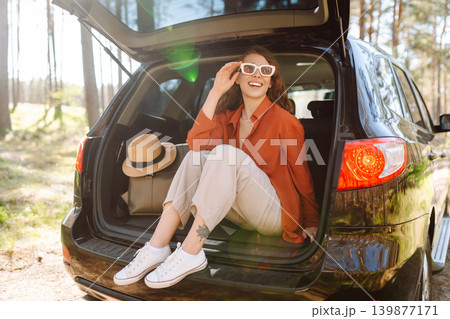 Road trips summer holidays. Woman enjoying nature while sitting in the trunk of her car Road trips summer holidays. Woman enjoying nature while sitting in the trunk of her car 139877171