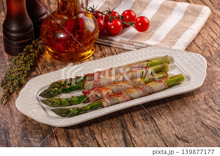 Savory grilled bacon wrapped asparagus spears on white platter with fresh herbs and tomatoes 139877177