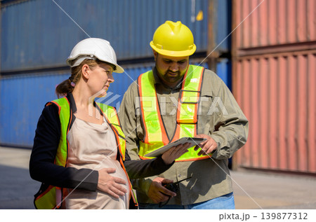 Diverse logistics team with pregnant female manager and male colleague worker reviewing data on tablet at shipping container yard port 139877312