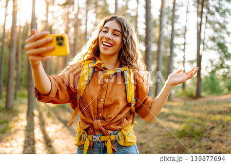 Selfie in nature. Beautiful woman taking picture of herself while walking in a sunny forest. Selfie in nature. Beautiful woman taking picture of herself while walking in a sunny forest. 139877694
