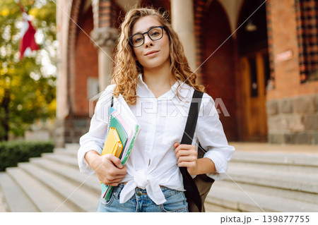 Female student woman holds several colorful notebooks near university building. Education concept. Female student woman holds several colorful notebooks near university building. Education concept. 139877755