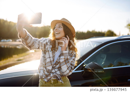 Happy woman on vacation taking selfie photo with smartphone near car. Stylish model on a car trip. 139877945
