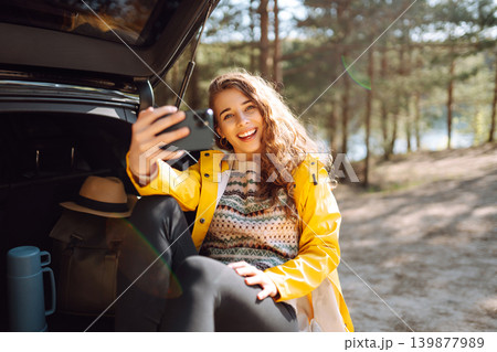 Woman is resting in trunk of car and taking selfie. Lifestyle, travel, tourism, nature, active life. 139877989