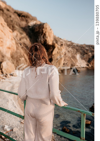 Coastline woman solitude standing by a railing overlooking the sea and rocky cliffs during a peaceful sunset at the beach Coastline woman solitude standing by a railing overlooking the sea and rocky cliffs during a peaceful sunset at the beach 139880705