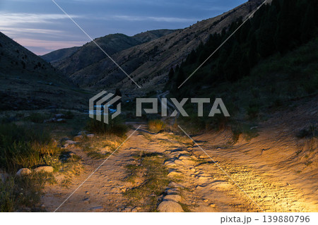 Dirt Road in Mountain Valley at Twilight illuminated with Headlights in Kyrgyzstan 139880796