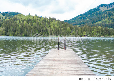 View from a wooden dock onto the calm surface of a mountain reservoir. Symmetry, perspective, travel concept, solitude, meditation, and serenity. View from a wooden dock onto the calm surface of a mountain reservoir. Symmetry, perspective, travel concept, solitude, meditation, and serenity. 139880815