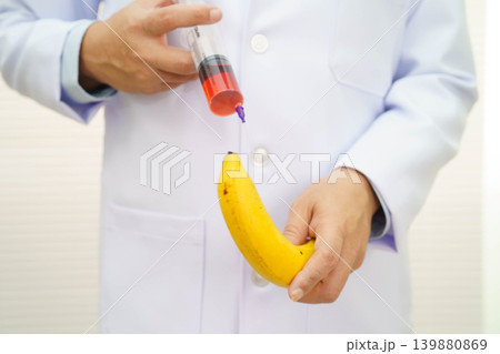 Male doctor making an injection to a banana with a syringe, penis health. Male doctor making an injection to a banana with a syringe, penis health. 139880869