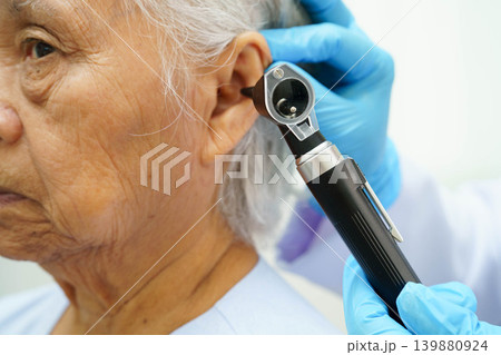 Otolaryngologist or ENT physician doctor examining senior patient ear with otoscope, hearing loss problem. 139880924