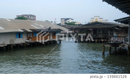 Wooden stilt houses built over calm water near a pier in a traditional coastal fishing village in Thailand. Waterfront village concept 139881526